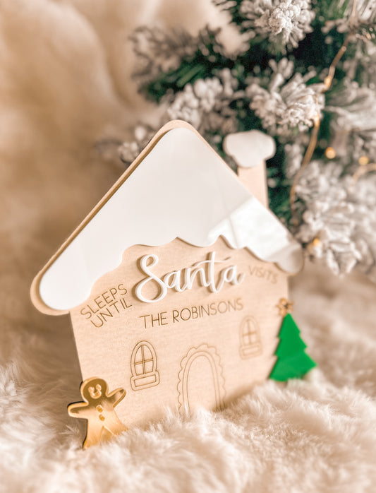 Decorative gingerbread house christmas countdown sign with 'Sleeps Until Santa Visits' text, Christmas tree in the background, wood and acrylic