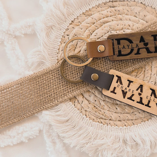 Two leather keychains with custom engraved text on a textured wooden surface, personalised key ring, gift for dad