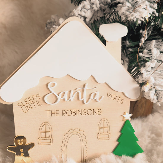 Decorative gingerbread house christmas countdown sign with 'Sleeps Until Santa Visits' text, Christmas tree in the background, wood and acrylic